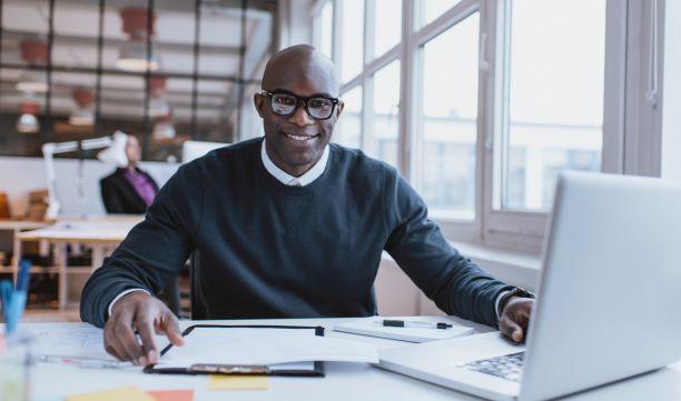 Professionally dressed man smiling at desk with laptop, documents, and reports on industrial security trends for 2024